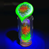 Andy G Puffco Peak top under a UV light, the Illuminati glowing green over rainbow line work