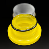 The canary yellow glass jar open, the black band around its threaded neck, the lid behind it