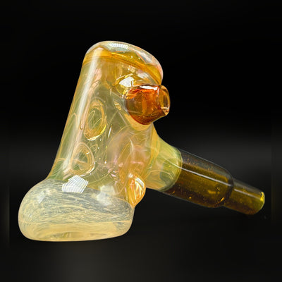Fumed glass hammer pipe by @itsnotawaterpipe, gold and silver fume with a Honey Badger stem, three-quarter view showing the carb and the can