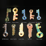 Ten hand blown glass key pendants by PyroVibe on a black background, each labeled with its color name