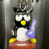 Close-up of a sculpted black and white bird character holding a purple beaker, on a stool inside the tube