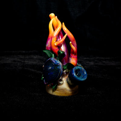 Turtle Glass reef sculpture pipe, orange and pink coral rising from a sandy base, on black.
