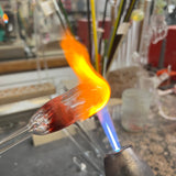 A glowing gather of hot glass swelling on the end of a tube in the torch flame at the High Tide Santa Barbara studio, where the Intro to Hollow Glass class is taught
